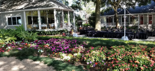 A garden with vibrant flowers in front of a house, featuring outdoor seating and a festive atmosphere.