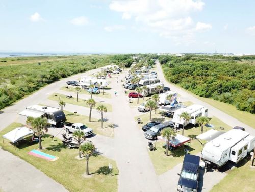 Aerial view of a busy RV park with multiple campers, vehicles, and palm trees under a clear blue sky.