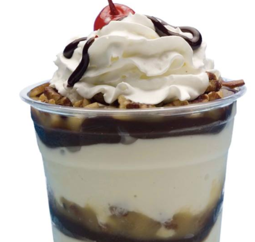 A delicious dessert cup with layers of vanilla ice cream, chocolate sauce, whipped cream, nuts, and a cherry on top.