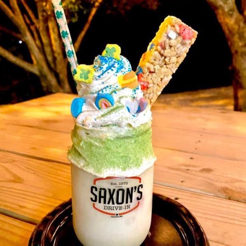 A colorful milkshake topped with whipped cream, sprinkles, candy, and a rice cereal treat, served in a jar.