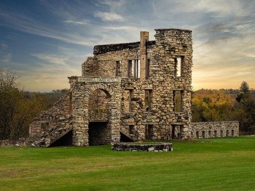 Ruins of a stone building with an archway, set against a colorful sky and green landscape.