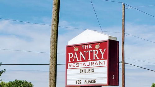 Sign for "The Pantry Restaurant" featuring the words "Skillets" and "Yes Please" against a blue sky.
