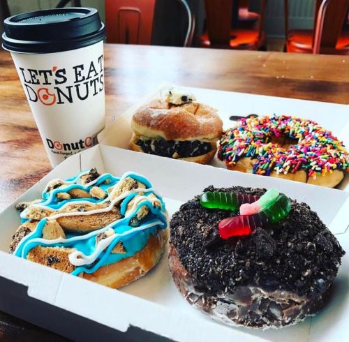 A box of colorful donuts with a coffee cup, featuring sprinkles, cookies, and gummy candies.