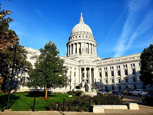 The Wisconsin State Capitol building with a large dome, surrounded by trees and a clear blue sky.