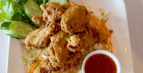 A plate of crispy fried chicken wings served with fresh vegetables and a small bowl of dipping sauce.