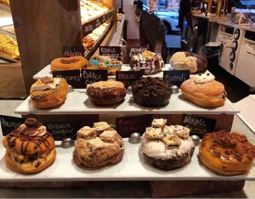 A display of assorted donuts on a tiered stand, featuring various flavors and toppings, with labels for each variety.