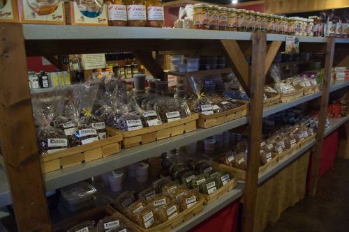 Shelves filled with various jars, baskets, and containers of food products in a rustic store setting.