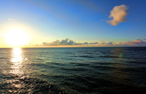 A serene ocean view at sunset, with vibrant colors reflecting on the water and clouds in the sky.