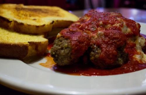 A plate featuring meatballs in marinara sauce alongside two slices of toasted bread.