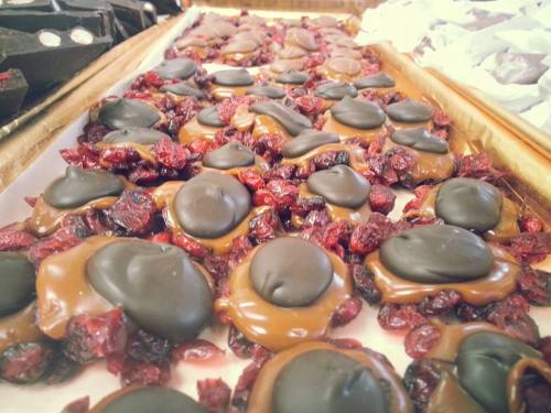 A close-up of chocolate-covered caramel candies topped with dried cranberries on a wooden tray.