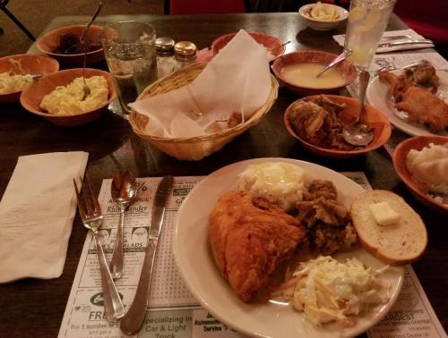 A table set with various dishes, including fried chicken, coleslaw, and sides, alongside drinks and utensils.