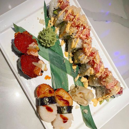 A plate of sushi featuring rolls, scallops, and strawberries, garnished with wasabi and ginger on a decorative leaf.