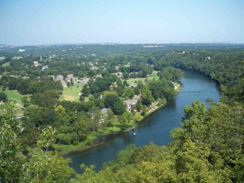 A scenic view of a river winding through lush greenery and homes, under a clear blue sky.