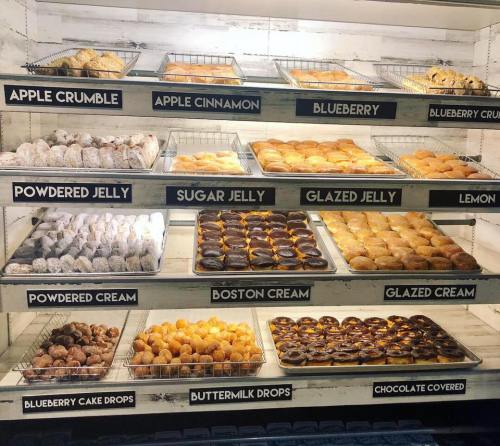 A display of various donuts and pastries, including jelly-filled, cream-filled, and flavored options, neatly arranged on shelves.
