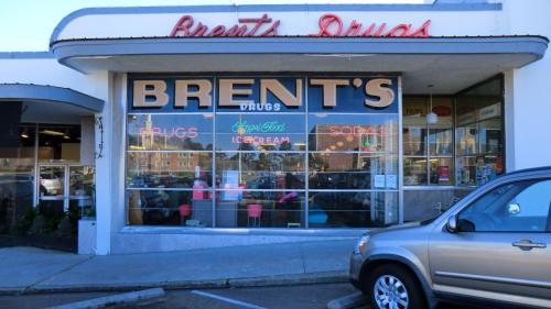 A storefront of Brent's Drugs featuring large windows displaying the name and offerings like ice cream and soda.