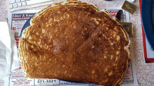A large, golden-brown pancake sits on a table covered with menus and syrup packets.