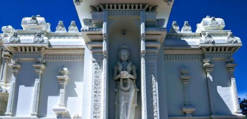 A white temple with intricate carvings and a statue of a deity at the entrance against a clear blue sky.