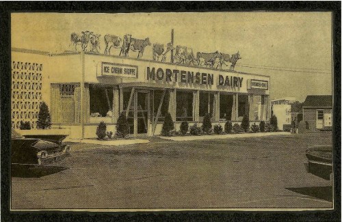 Historic image of Mortensen Dairy, featuring a storefront with cows on the roof and a classic car parked outside.