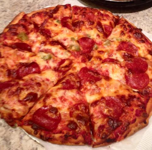 A freshly baked pepperoni pizza with melted cheese and green peppers, sliced into eight pieces on a countertop.