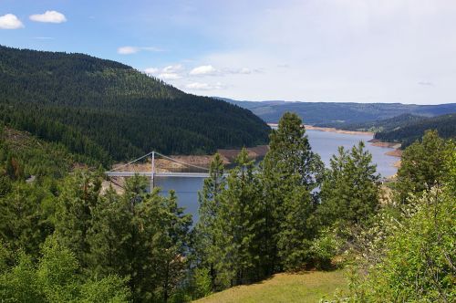 A scenic view of a lake surrounded by green hills and trees, with a bridge spanning across the water.
