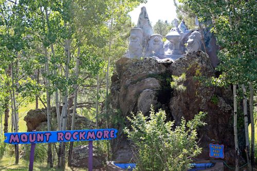 A whimsical rock formation resembling Mount Rushmore, surrounded by trees, with a colorful sign reading "Mount Rockmore."