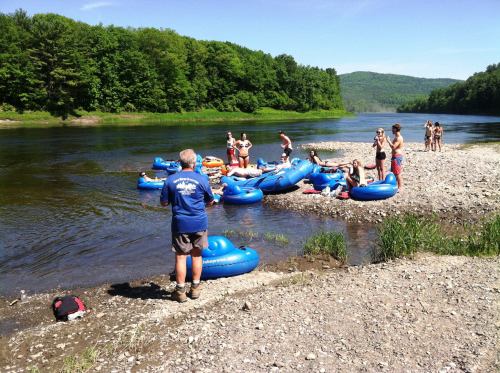 A group of people enjoying a sunny day by a river, with blue inner tubes scattered along the shore.