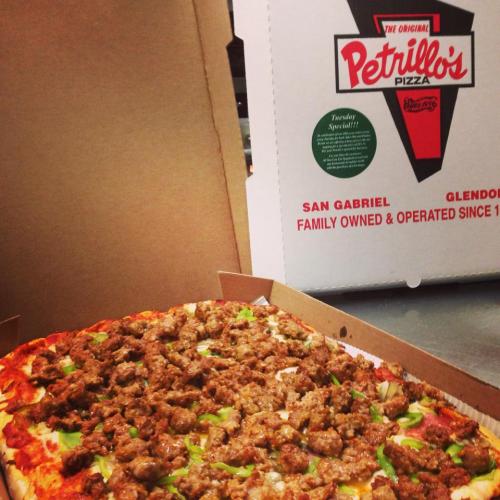 A large pizza topped with sausage and green peppers, next to a box from Petrillo's Pizza, family-owned since 1971.