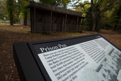 Sign describing the Prison Pen at Camp Hoffman, a Confederate prison camp during the Civil War, with a wooden structure in background.