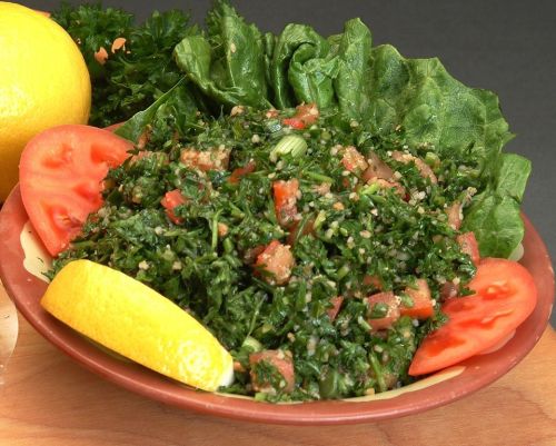 A vibrant salad featuring chopped parsley, tomatoes, and lemon, served in a bowl with lettuce and lemon wedges.