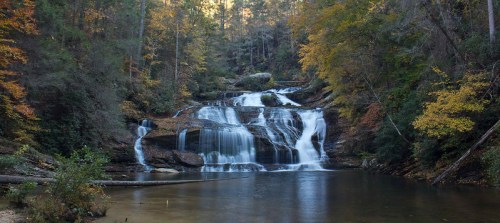 A serene waterfall cascades over rocks into a calm pool, surrounded by autumn foliage and lush greenery.