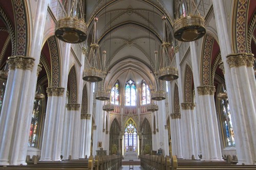 Interior of a grand church featuring tall arches, ornate chandeliers, and colorful stained glass windows.