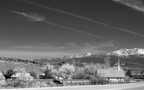 A black and white landscape featuring a church, a house, and mountains under a cloudy sky.