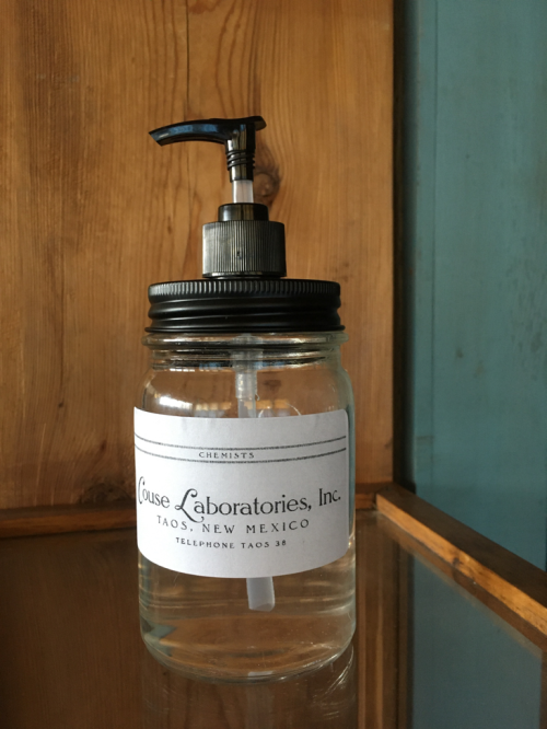 A glass jar with a pump lid, labeled "Couse Laboratories, Inc." from Taos, New Mexico, containing a clear liquid.