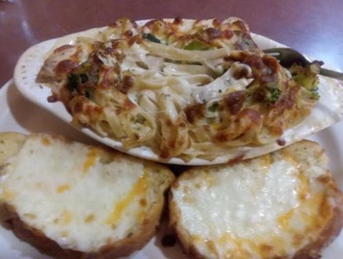 A creamy pasta dish with broccoli, baked and topped with cheese, served with two slices of cheesy garlic bread.