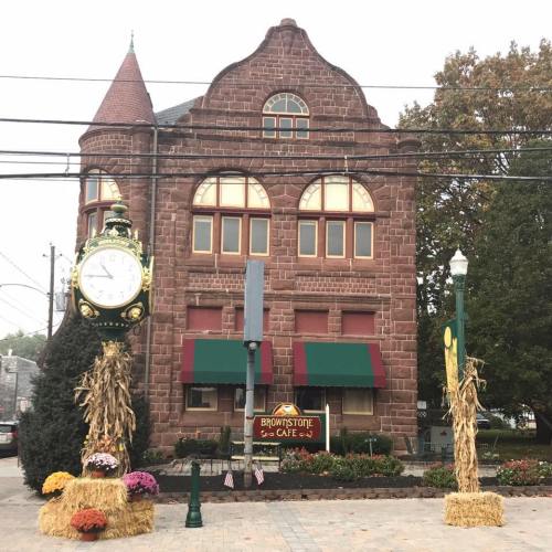 Historic brick building with a clock, sign for Brownstone Cafe, and autumn decorations including hay and flowers.