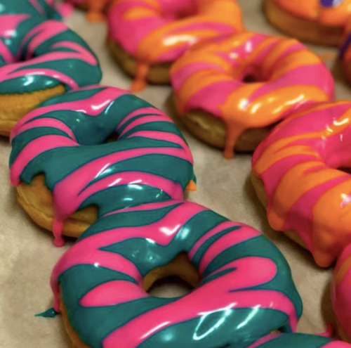 Colorful donuts with vibrant pink and teal icing, arranged on a parchment-lined tray.