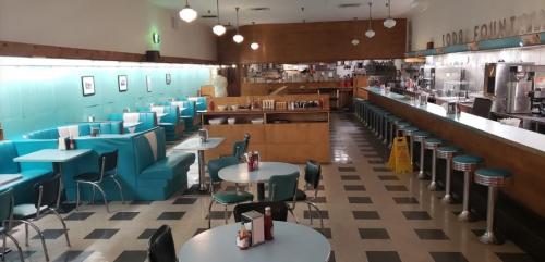Retro diner interior with teal booths, round tables, and a long counter with stools, featuring a classic 1950s vibe.