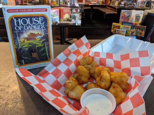 A basket of golden fried snacks with a side of dipping sauce, next to the game "House of Danger" on a table.