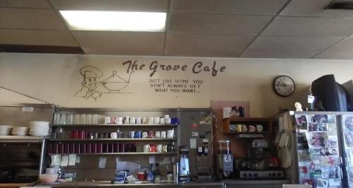 Interior of The Grove Cafe, featuring a wall sign, shelves with dishes, and a clock. Cozy diner atmosphere.