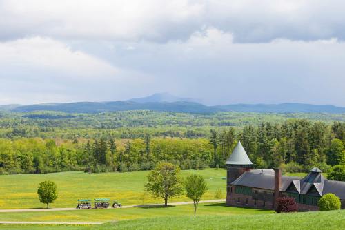A scenic view of rolling green hills, a stone building with a tower, and distant mountains under a cloudy sky.