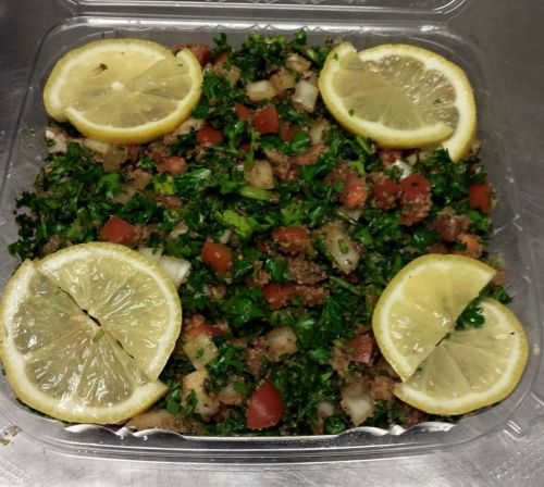 A container of tabbouleh salad topped with lemon slices, featuring parsley, tomatoes, and bulgur wheat.