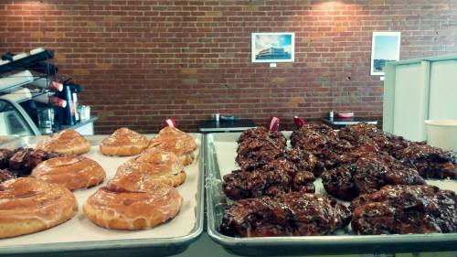 Two trays of pastries: glazed donuts on the left and chocolate-covered cookies on the right, set against a brick wall.
