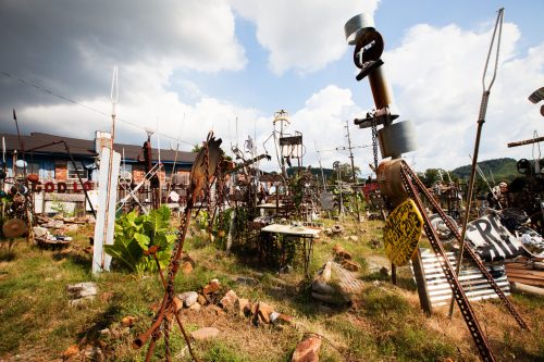A whimsical outdoor art installation featuring various metal sculptures and structures amidst grassy terrain under a cloudy sky.