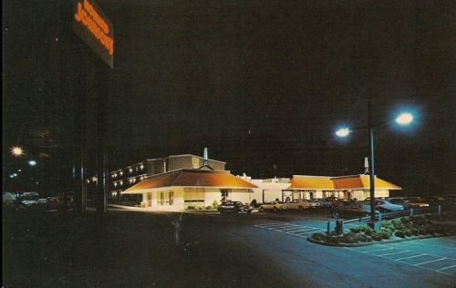 A retro diner at night, featuring bright orange roofs, parking lot, and illuminated signage.