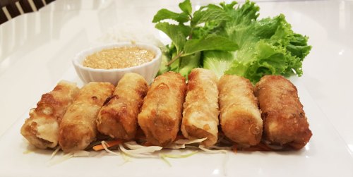 A plate of crispy spring rolls served with fresh lettuce, herbs, and a small bowl of dipping sauce.