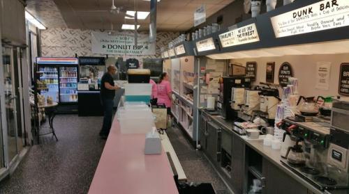 A retro-style diner with a long counter, coffee machines, and a customer being served by a staff member.