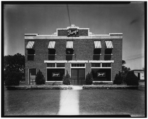 Historic brick building with striped awnings and "Barg's" signage, surrounded by neatly trimmed grass and shrubs.