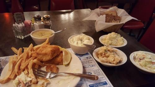 A table set with fried fish, fries, coleslaw, and various dips, alongside a basket of bread in a cozy restaurant.