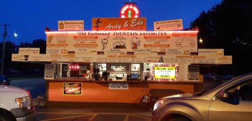 A brightly lit drive-in restaurant with a colorful menu board, featuring classic diner food and ice cream options.