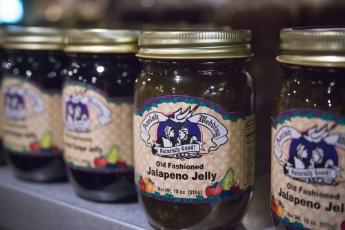 Four jars of Old Fashioned Jalapeno Jelly with colorful labels, lined up on a shelf.
